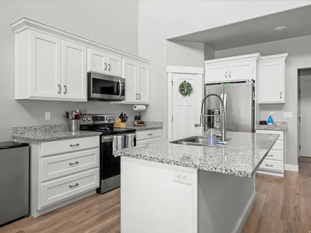 Modern kitchen featuring white shaker cabinetry with crown molding, stainless steel appliances, granite countertops, wood-finish flooring, and a kitchen island with an integrated sink