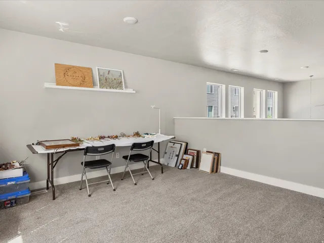 Spacious loft area featuring light gray walls, plush gray carpeting, and multiple windows providing ample natural light