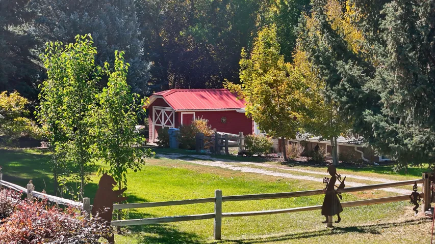 Red barn with white trim and a vibrant red roof, framed by mature trees