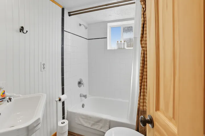 Bathroom featuring a white pedestal sink, white subway tile shower surround with black accent tile, and a single window above the bathtub