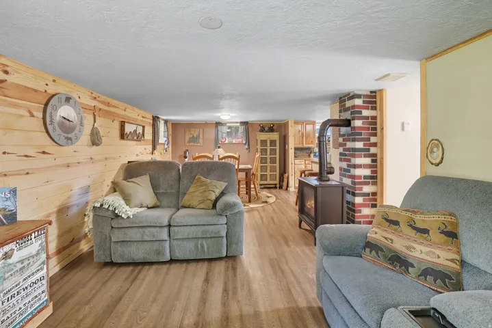 Spacious recreation room featuring wood-finish flooring, a wood-burning stove with a brick surround, and knotty pine paneling