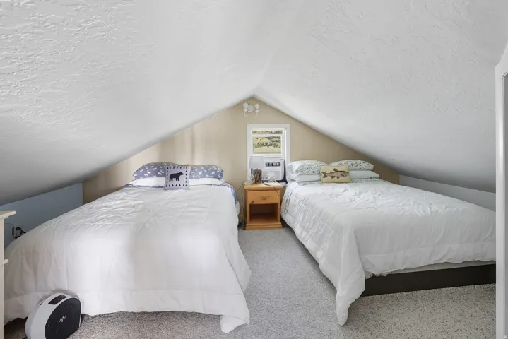 Attic space featuring sloped ceilings, textured white walls, and light-colored carpeting