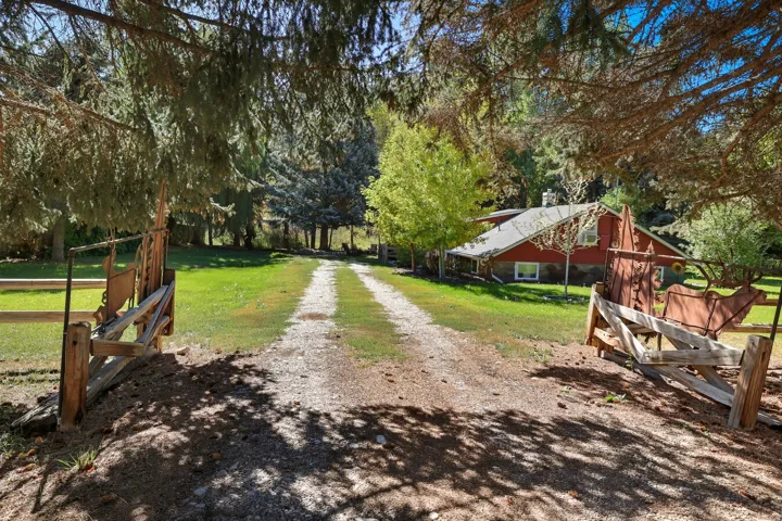 Gated entry with a gravel driveway leading to a red-sided residence featuring a gray roof