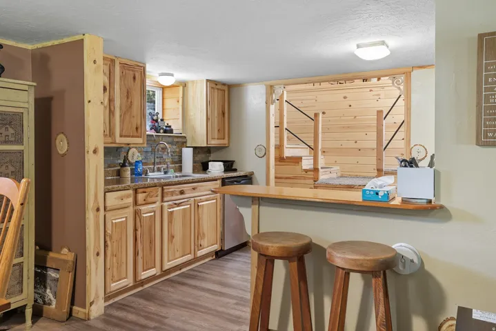 Kitchenette featuring natural wood cabinetry, stone-look backsplash, a stainless steel sink, and a built-in breakfast bar