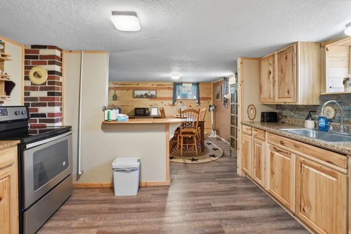 Kitchen featuring wood-finish flooring, natural wood cabinetry, a stainless steel electric range, and a stone-look backsplash