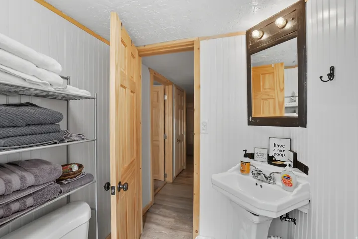 Bathroom featuring a pedestal sink, wall-mounted mirror with integrated lighting, and beadboard paneling