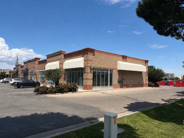 Multi-unit commercial building featuring brick and stone-look facade, multiple storefronts with large glass panels, individual awnings, and an asphalt parking lot