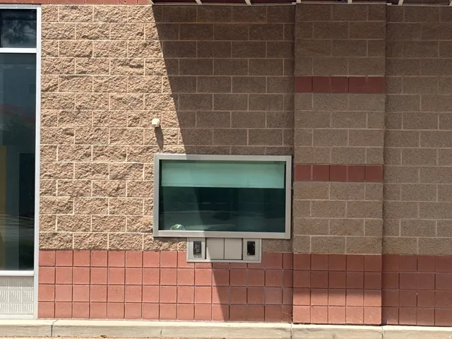 Exterior featuring textured block masonry, a large commercial window with aluminum framing, and a drive-thru service window with a speaker system