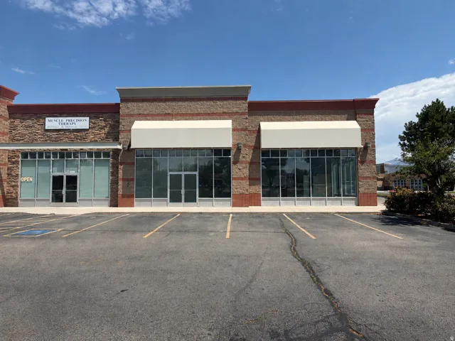Commercial building exterior featuring brick-clad facade with stone accents, multiple storefront windows, and two retractable awnings