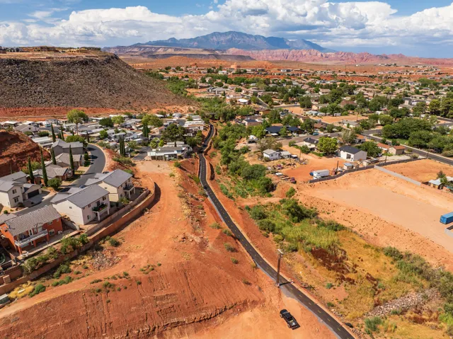 Expansive elevated landscape featuring developed properties, raw land, a paved pathway, and distant mountain ranges