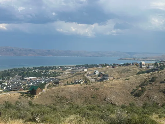 Expansive hillside property featuring panoramic lake and mountain scenery, with a town visible along the shoreline