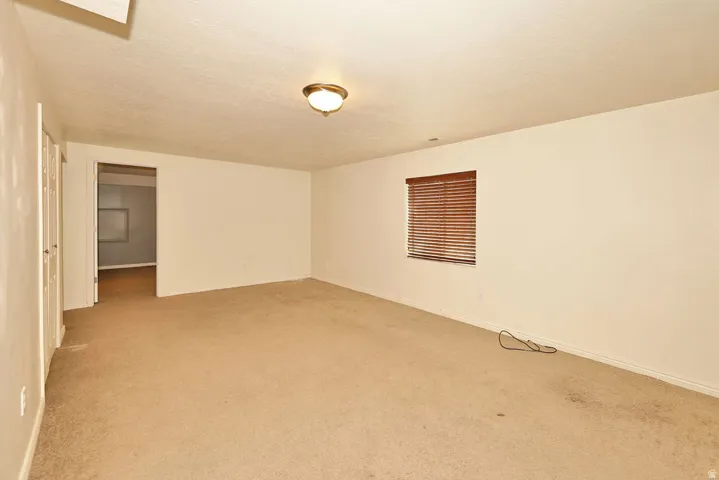 Carpeted room featuring a ceiling-mounted light fixture, a window with wood-finish blinds, and a doorway to an additional interior space