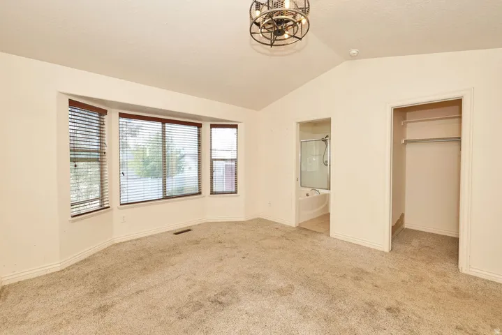Spacious room featuring a vaulted ceiling and a bay window with blinds