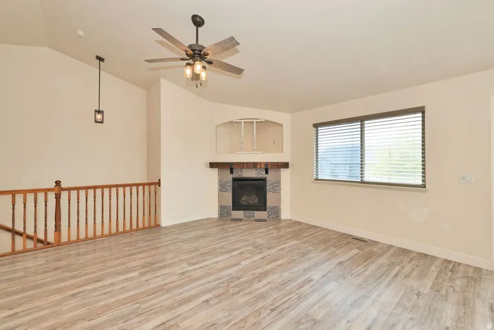 Spacious living area featuring wood-finish flooring, a ceiling fan with integrated lighting, and a fireplace with a decorative tile surround and wood mantel