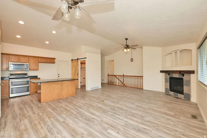 Open-concept living space featuring wood-finish flooring, a kitchen island with dark countertop, stainless steel appliances, and a fireplace with tile surround