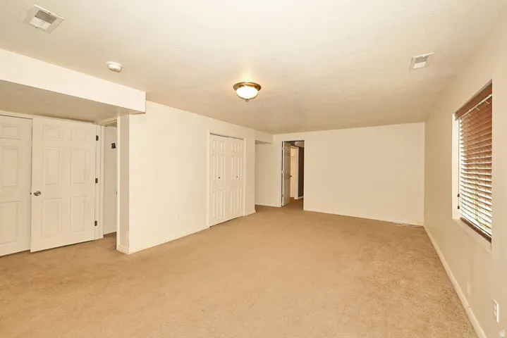 Carpeted room featuring multiple white paneled doors, a window with horizontal blinds, and a flush mount ceiling light fixture