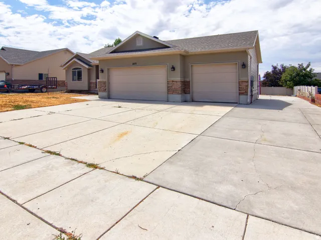 Contemporary stucco exterior with a multi-car garage, stone veneer accents, and a concrete driveway