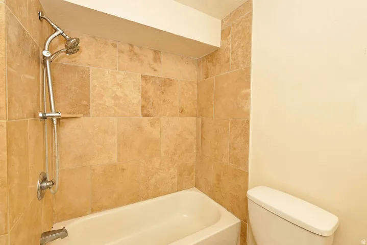 Tub and shower combination with natural stone-look wall tiles, chrome fixtures, and a handheld shower head