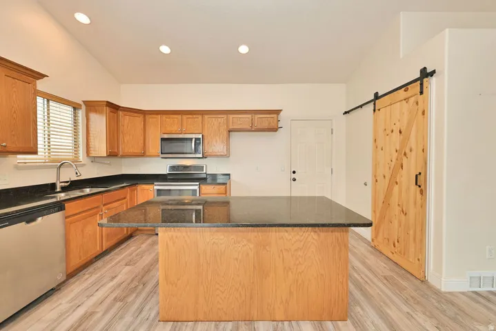 Kitchen featuring wood cabinetry, stainless steel appliances, dark countertops, a central island, and wood-finish flooring