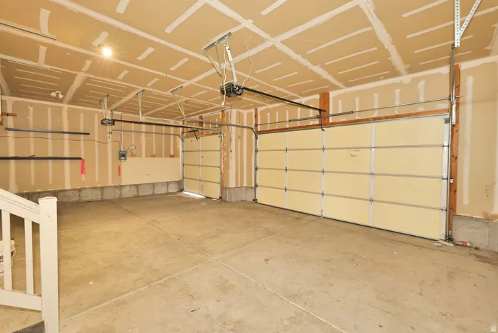 Spacious garage featuring two overhead doors, concrete flooring, exposed wood framing, and overhead lighting
