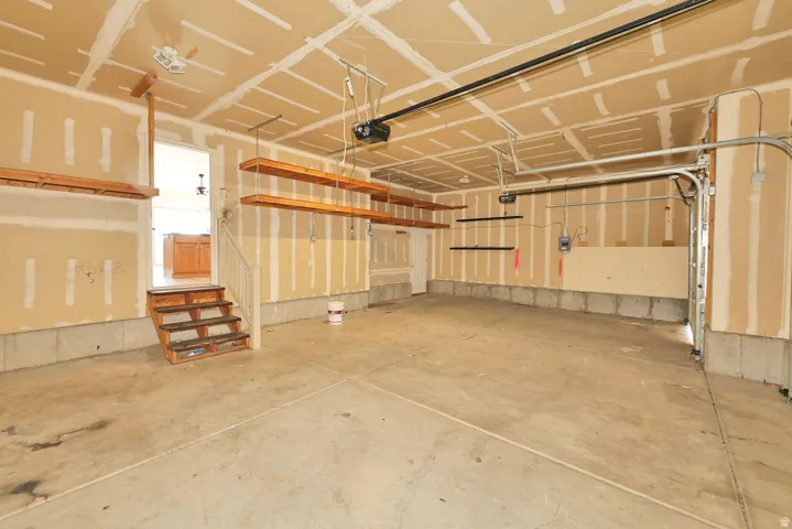 Spacious garage featuring a concrete floor, overhead shelving, exposed wall studs, and a garage door opener system