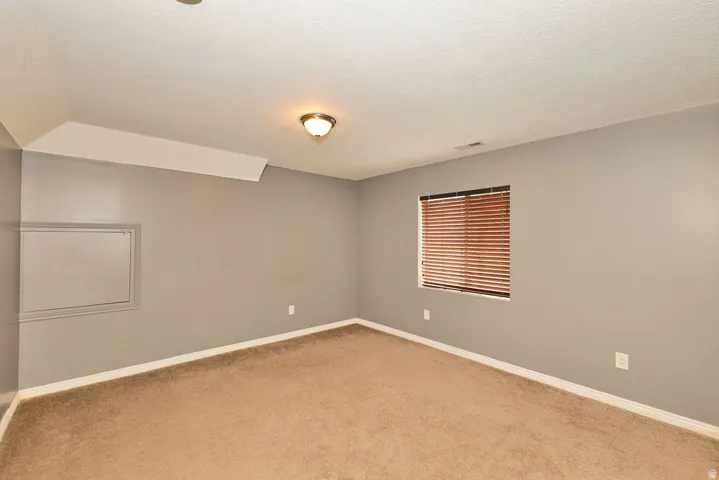 Carpeted room featuring neutral wall paint, white baseboards, and a window with wood-tone blinds