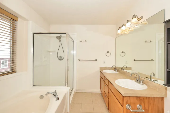 Bathroom featuring a glass-enclosed shower, built-in soaking tub, and a dual-sink vanity with wood cabinetry