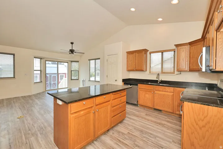 Kitchen featuring a central island with a dark countertop, wood cabinetry, stainless steel dishwasher, and recessed lighting