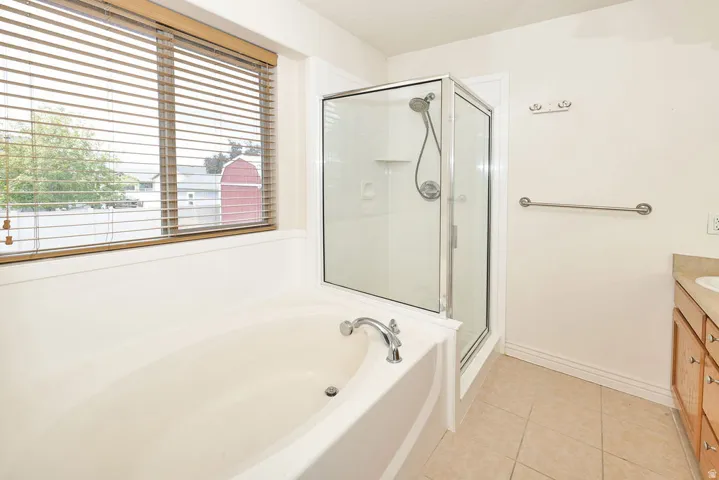Bathroom featuring a corner shower enclosure, a built-in soaking tub with chrome fixtures, and a window with wood-finish blinds