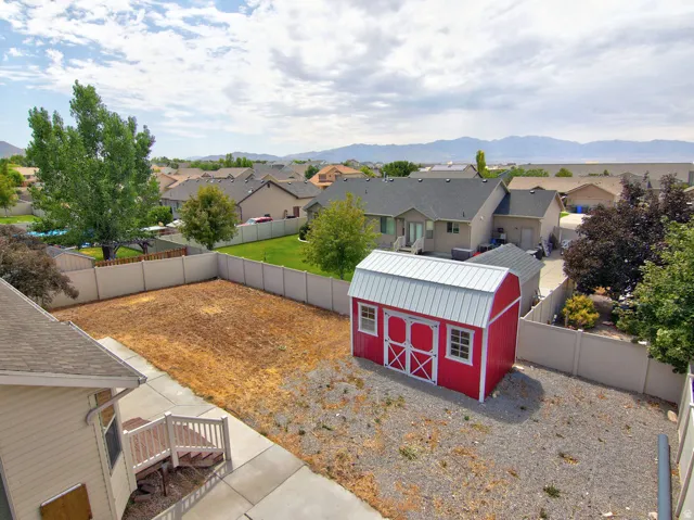 Spacious backyard featuring a red barn-style shed with a metal roof and double doors, a white privacy fence, and a concrete patio with stairs