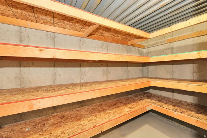 Utility room with concrete block walls, multi-level wood shelving, and a corrugated metal ceiling