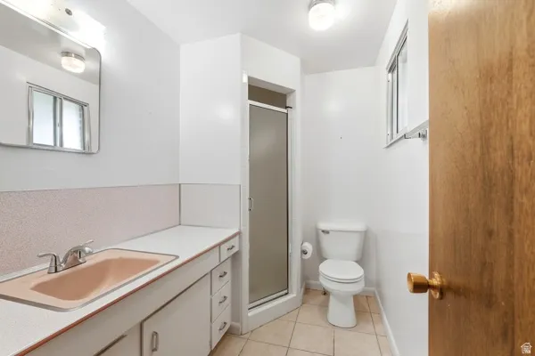 White bathroom featuring a built-in vanity with an integrated sink, a shower enclosure with frosted glass, a toilet, a window, and tiled flooring