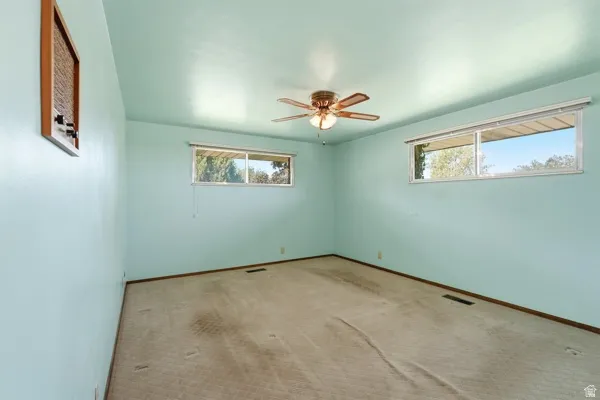 Room with light blue walls, beige carpet, and multiple windows