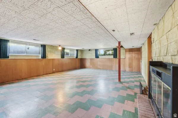 Spacious lower level featuring a fireplace with a brick hearth, wood-paneled walls, and a patterned tile floor