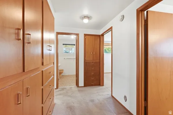 Hallway featuring extensive built-in wood cabinetry, light-toned carpeting, white walls, and wood-trim doorways