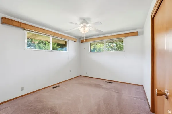 Neutral tone carpeted room featuring a white ceiling and walls, two windows with wood valances, a ceiling fan with light fixture, and a wood-finish door