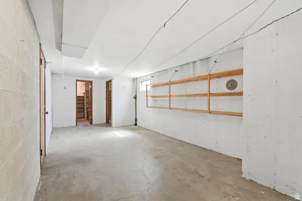 Spacious unfinished basement offering concrete flooring, painted cinder block walls, exposed joists, and overhead lighting
