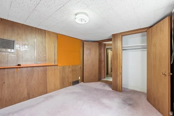 Room featuring wood paneling, ceiling-mounted light fixture, wall-to-wall carpeting, bi-fold closet doors, and built-in shelving