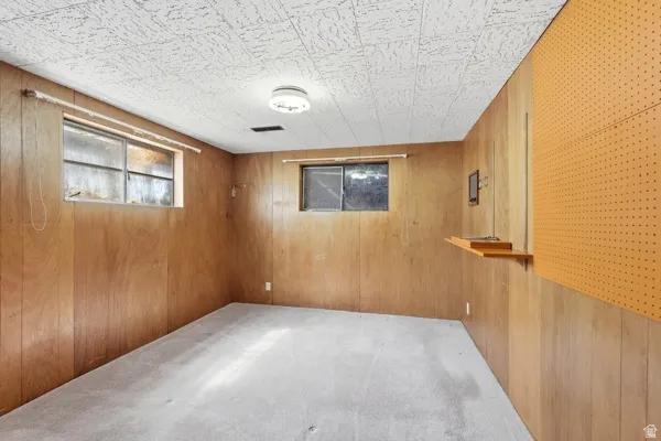 Room featuring wood-paneled walls, a drop ceiling, and light-colored carpeting