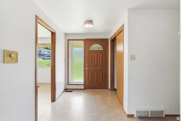 Entryway featuring a wood-panel door with an arched glass insert, sidelight with textured glass, and light-toned tile flooring