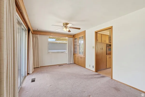 Spacious room featuring light-toned carpeting, a ceiling fan with integrated lighting, and a large sliding glass door