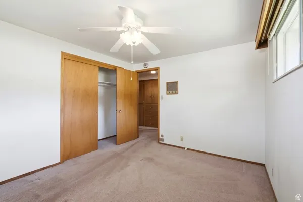 Carpeted room featuring a ceiling fan with integrated lighting, a window with an integrated blind, and a wood-finish bi-fold closet