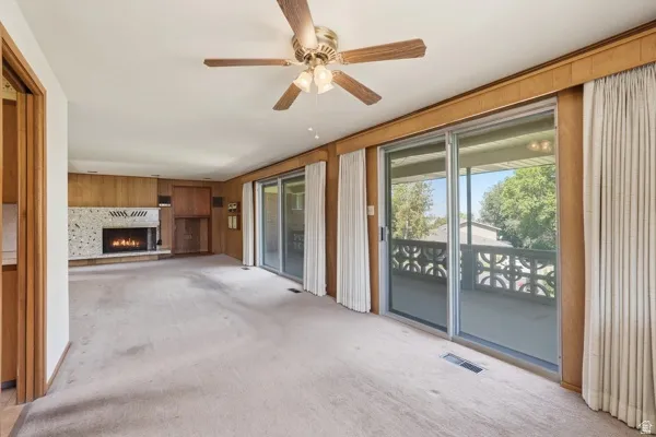 Spacious interior with carpet flooring, a stone-surround fireplace, wood paneling, and a ceiling fan