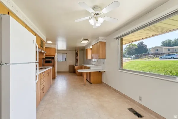 Kitchen featuring light wood cabinetry, white countertops, built-in oven, and a white refrigerator