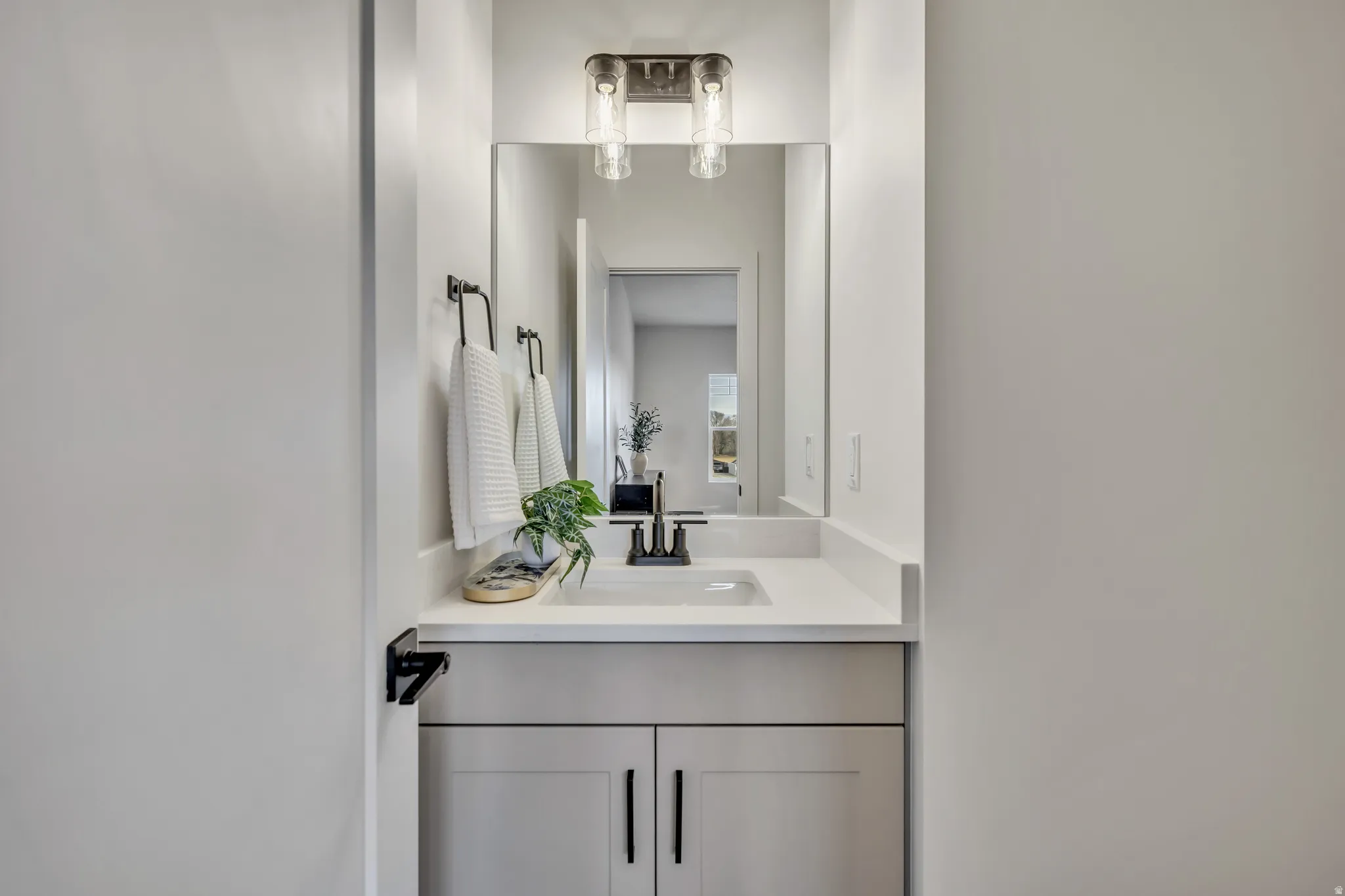 Bathroom vanity featuring a light gray cabinet, white countertop, rectangular undermount sink, matte black faucet, and coordinating towel ring