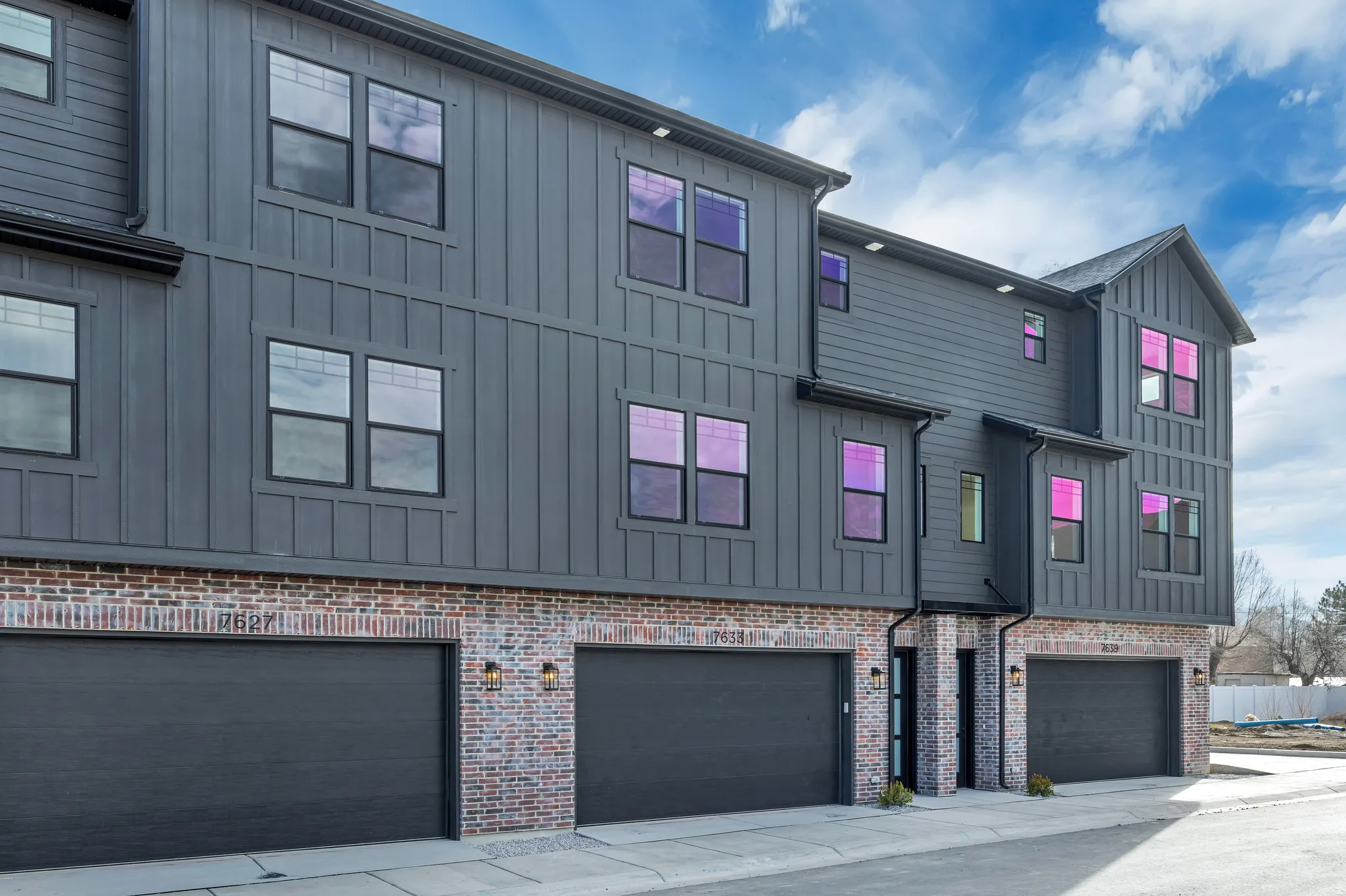 Contemporary multi-story exterior featuring dark vertical siding and a brick base