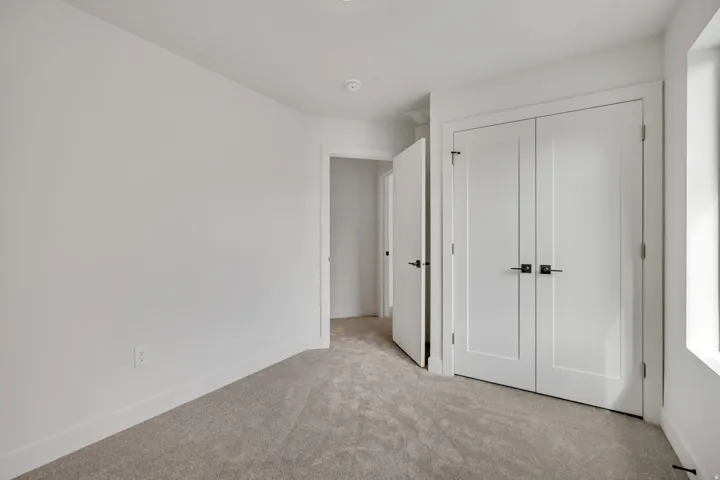 White paneled closet doors with contemporary hardware complement the light gray carpeting