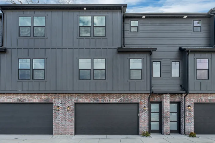 Modern multi-story exterior featuring a gray vertical board and batten siding, horizontal siding, and a brick facade