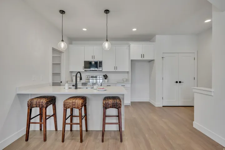 Open-concept kitchen featuring an island with counter seating, pendant lighting, white cabinetry, and stainless steel appliances