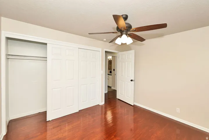 Spacious room featuring wood-finish flooring, a ceiling fan with integrated lighting, and a large closet with sliding panel doors